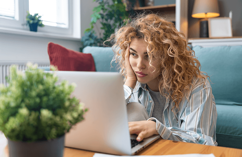 Junge Frau mit lockigem Haar sitzt müde und frustriert vor einem Laptop im Wohnzimmer – Ausdruck von mentaler Erschöpfung oder Schwierigkeiten beim Fokussieren.