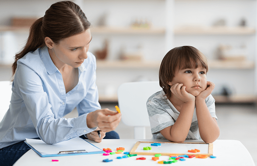 Mutter versucht, die Aufmerksamkeit eines kleinen Jungen beim Spiel mit bunten Lernsteinen zu gewinnen, während der Junge desinteressiert zur Seite schaut – Szene für ADS.