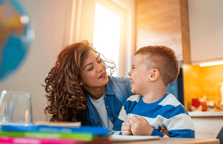 Mutter und Sohn lachen sich liebevoll an, während sie gemeinsam am Tisch sitzen – Symbol für emotionale Nähe und unterstützendes Familienumfeld.
